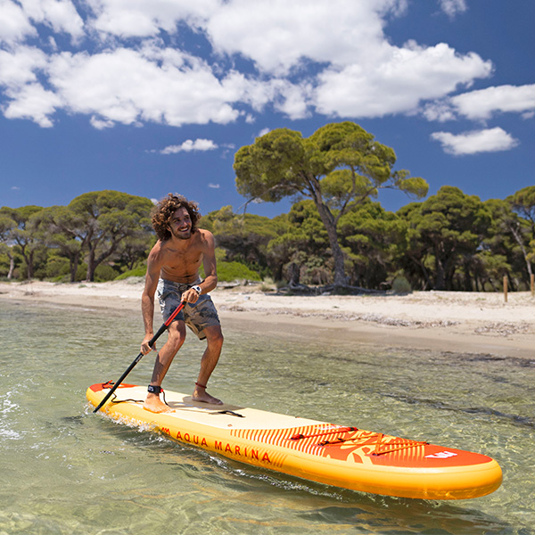 Eine Person auf Aqua Marina Fusion 2026 SUP Boards am Strand; klares Wasser und sonnige Outdoor-Szene Einsätze auf Seen und Küsten.