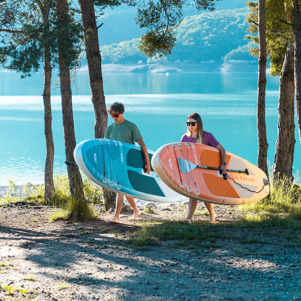 Lifestyle: Zwei Personen mit Aqua Marina Halo und Airo SUP Boards am Strand unter Palmen; klares Wasser und sommerliche Outdoor-Szene